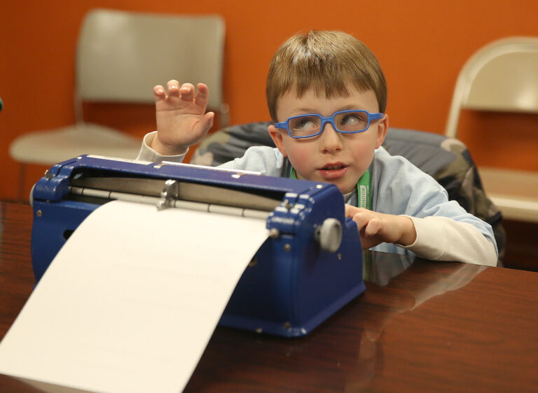 image of young boy with blue glasses typing on a brailler