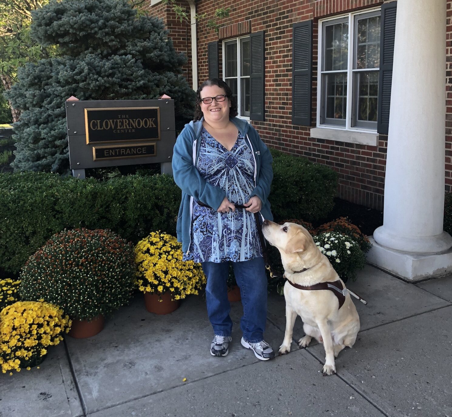 Photo of staff - Deanna Lewis in front of Clovernook sign with her guide dog Mambo