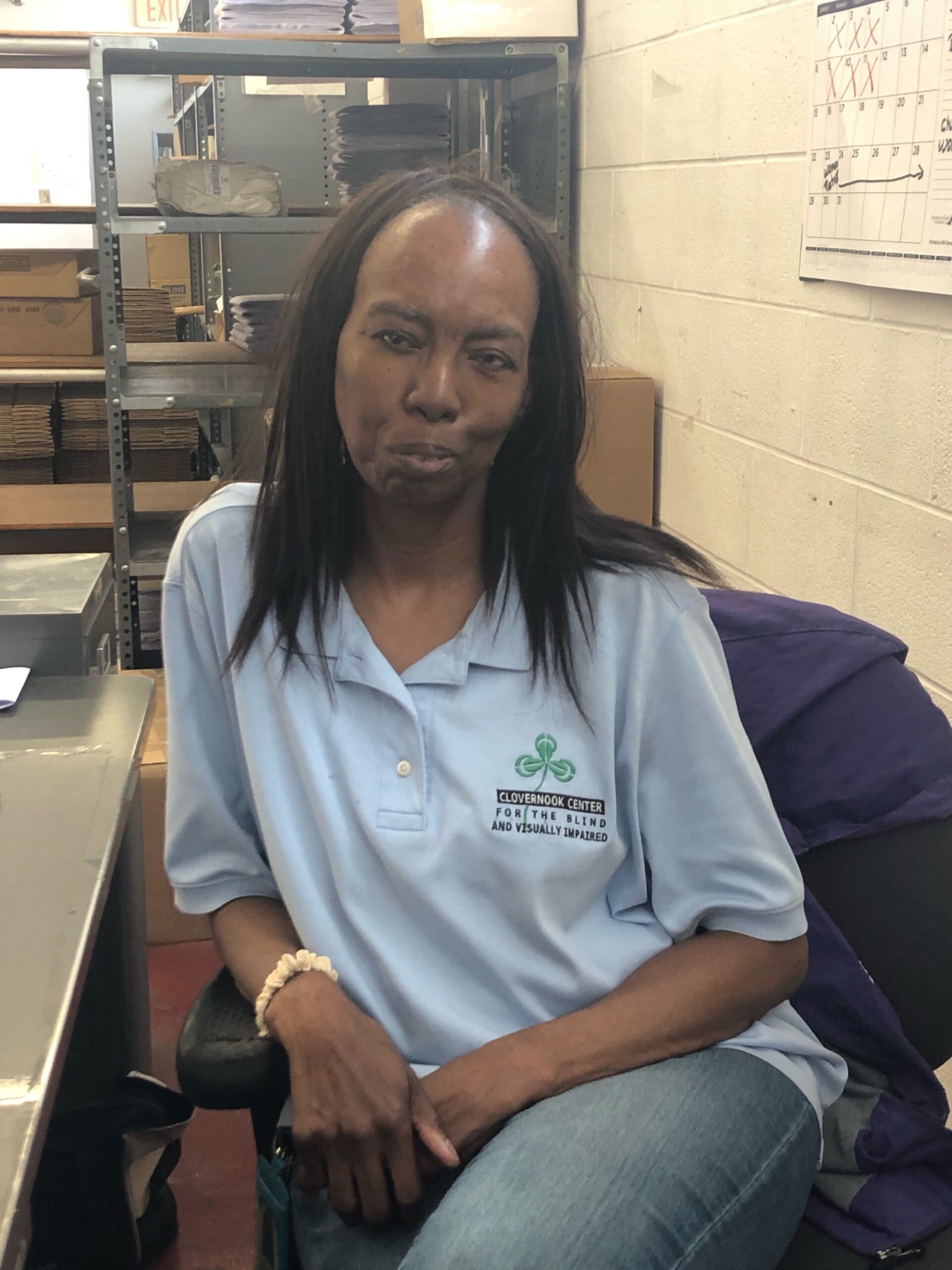 Image of Barb Easterling sitting at her station in the braille department looking at the camera