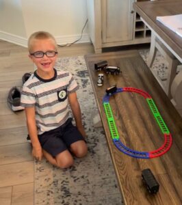 Isaac sitting next to a toy train set