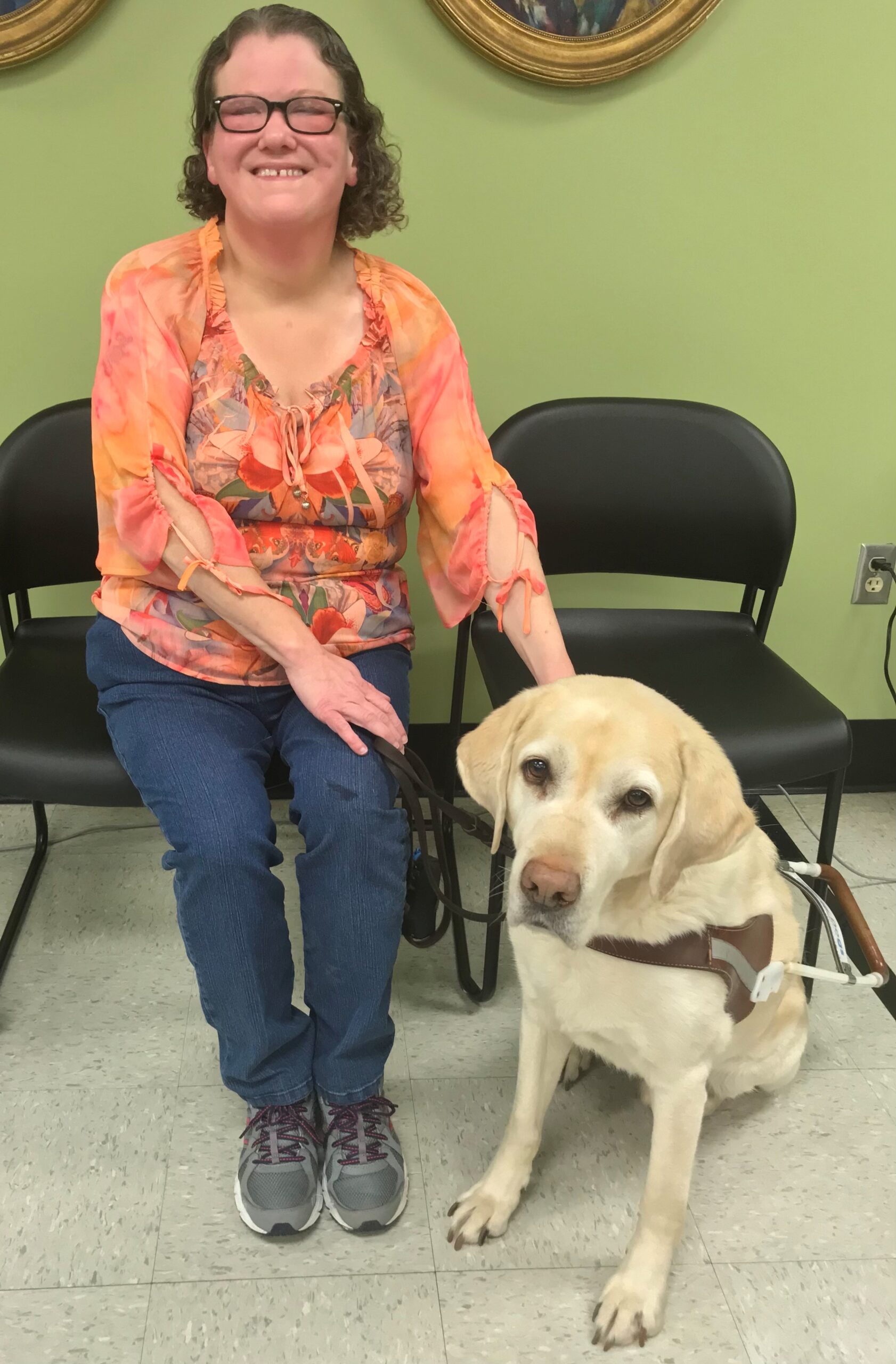 Deanna sitting in chair and smiling with Mambo sitting next to her on the floor