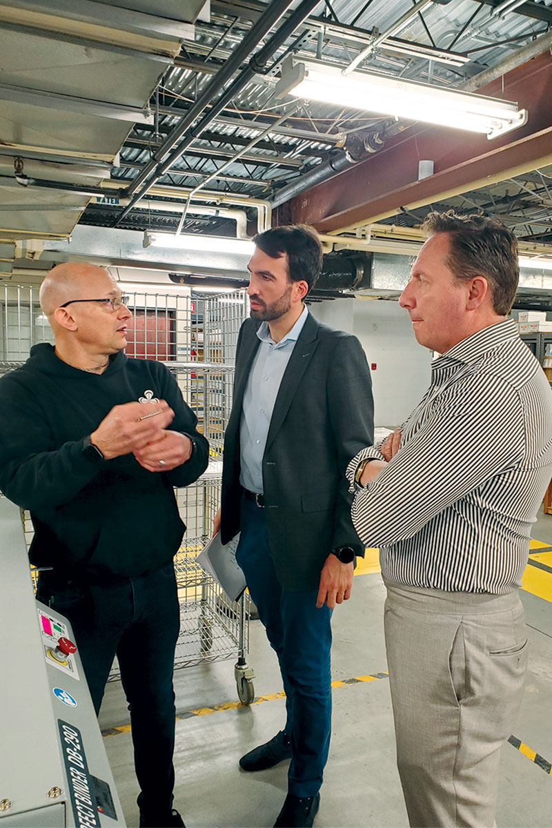 Eurostampa Senior Innovation Manager Ermanno Bosco-Orsi and CEO Gianmario Cillario visit the Clovernook printing house.Three men stand talking next to the new binding machine.