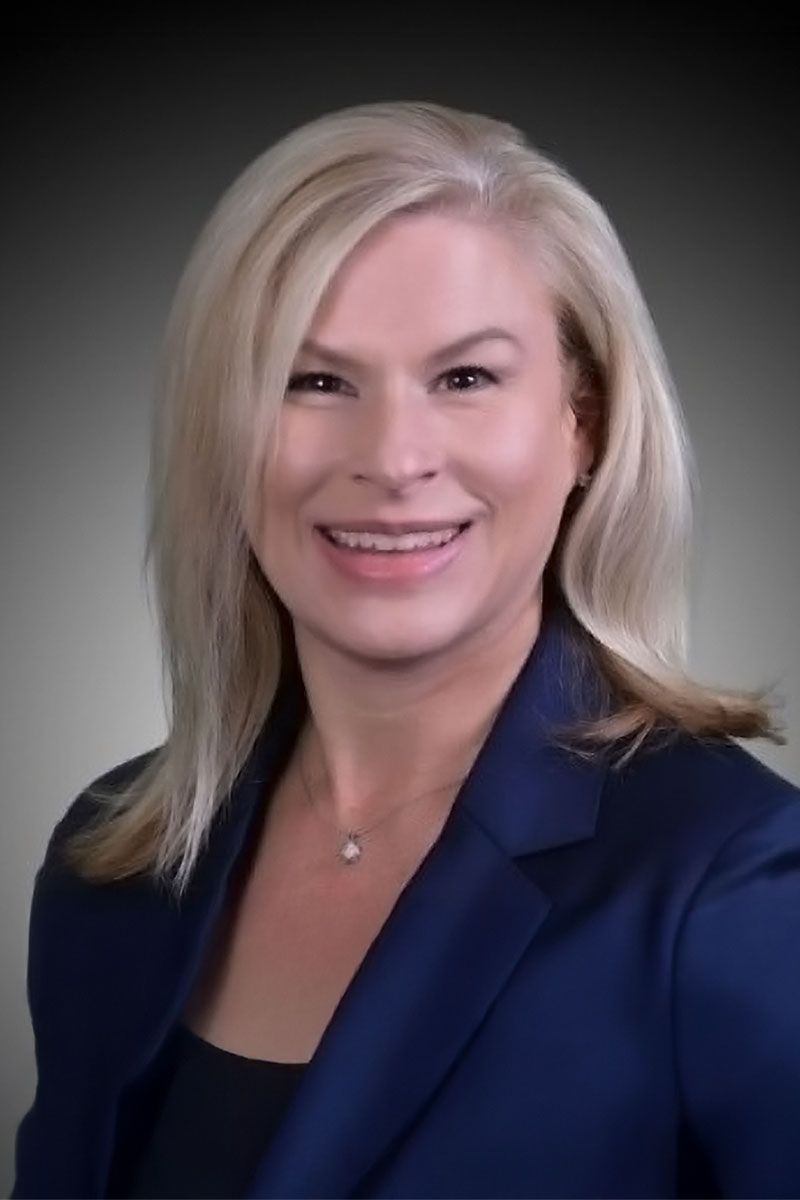 A portrait photo of Jennifer DuBois, a woman with straight blonde hair wearing a navy blazer.