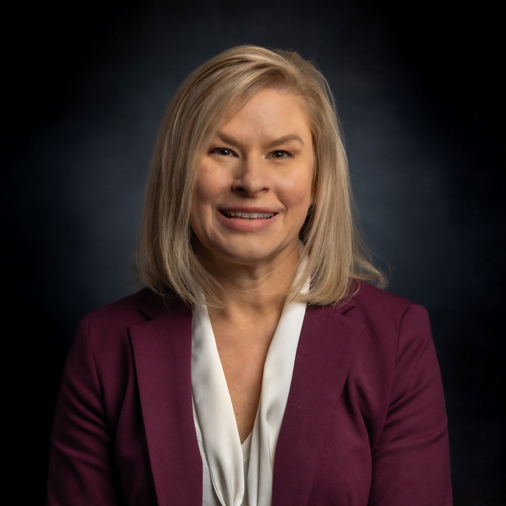 Jennifer DuBois has blond, shoulder length hair and is wearing a plum suit jacket.