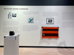 a photo of one of the walls of the Tactile Revolutions exhibit. This text on the wall highlights Clovernook Center's history as a braille printing house. There are multiple tactile artifacts available to hold and feel